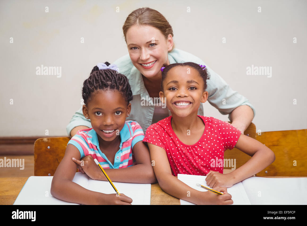 Cute pupils and teacher smiling at camera in classroom Stock Photo - Alamy