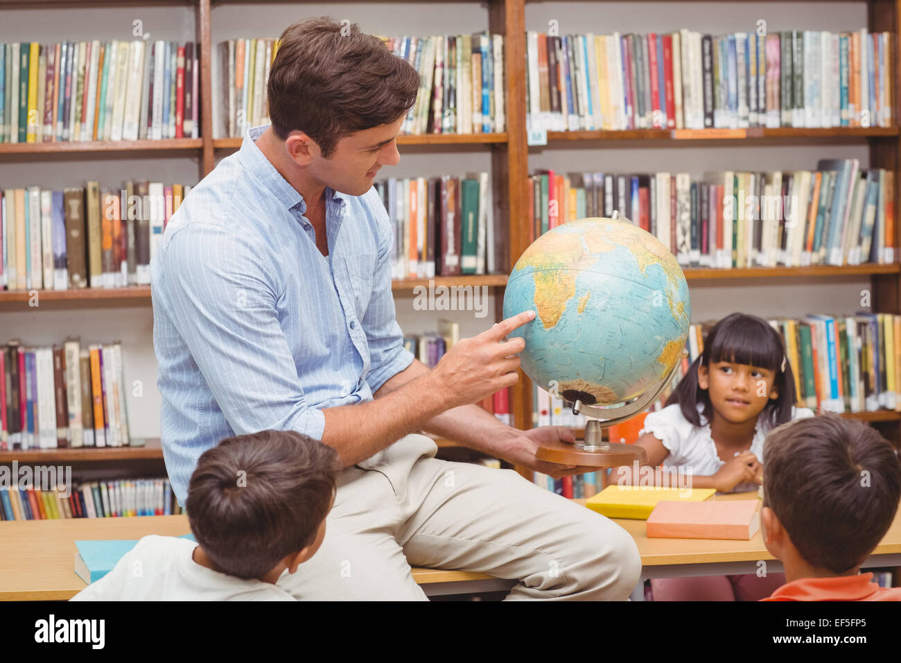 Cute pupils and teacher looking at globe in library Stock Photo - Alamy