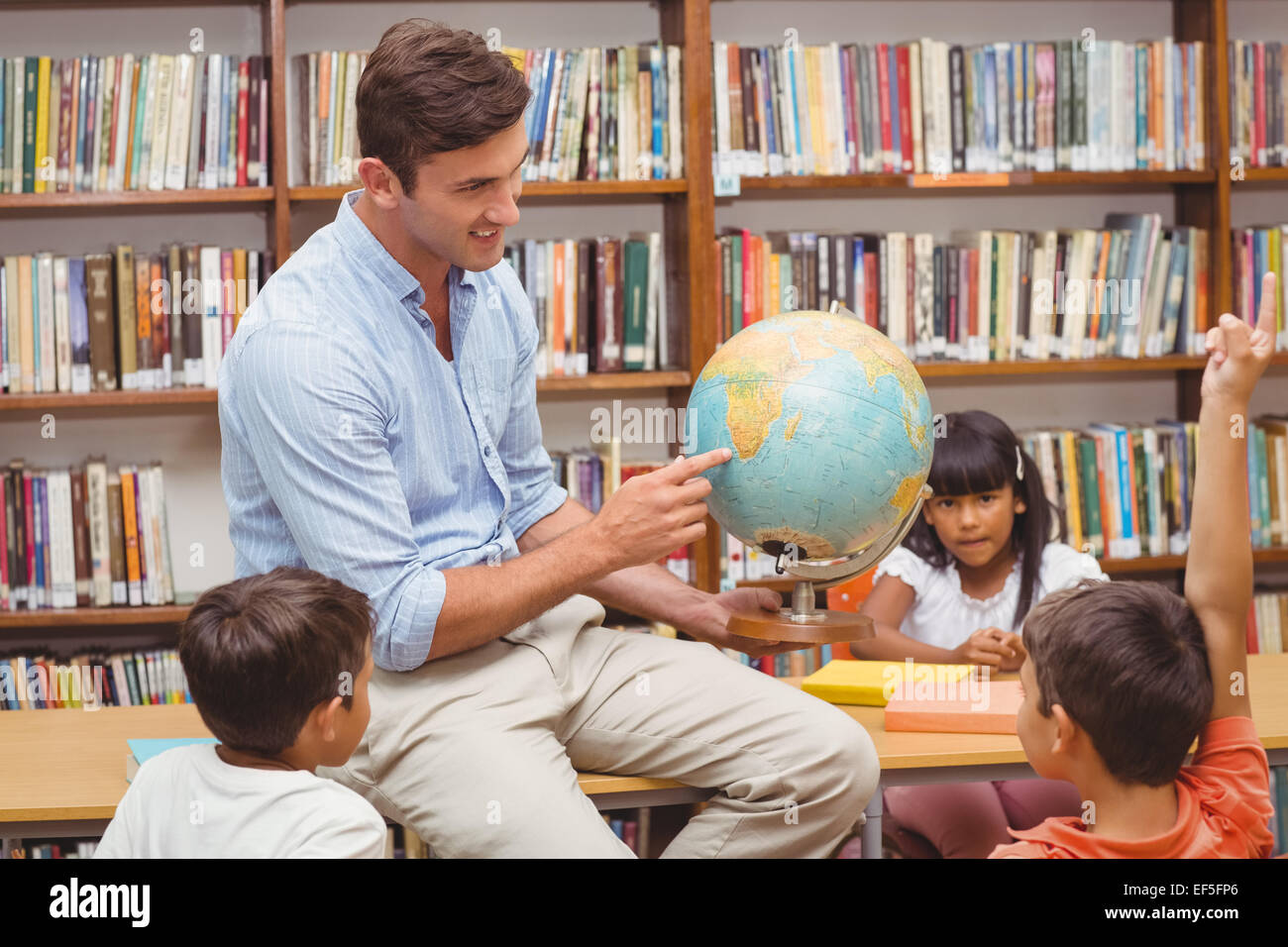 Cute pupils and teacher looking at globe in library Stock Photo - Alamy