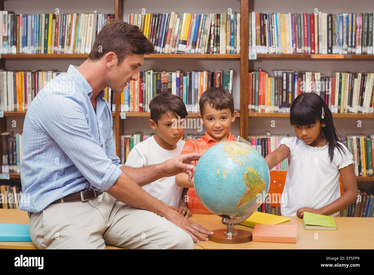 Cute pupils and teacher looking at globe in library Stock Photo - Alamy