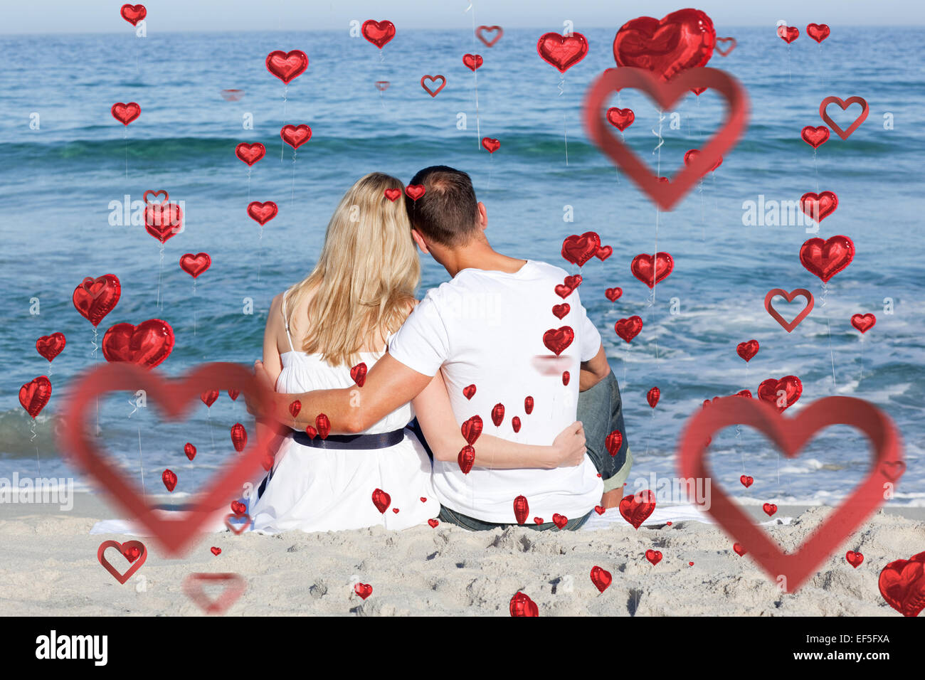 Composite image of affectionate couple sitting on the sand at the beach Stock Photo