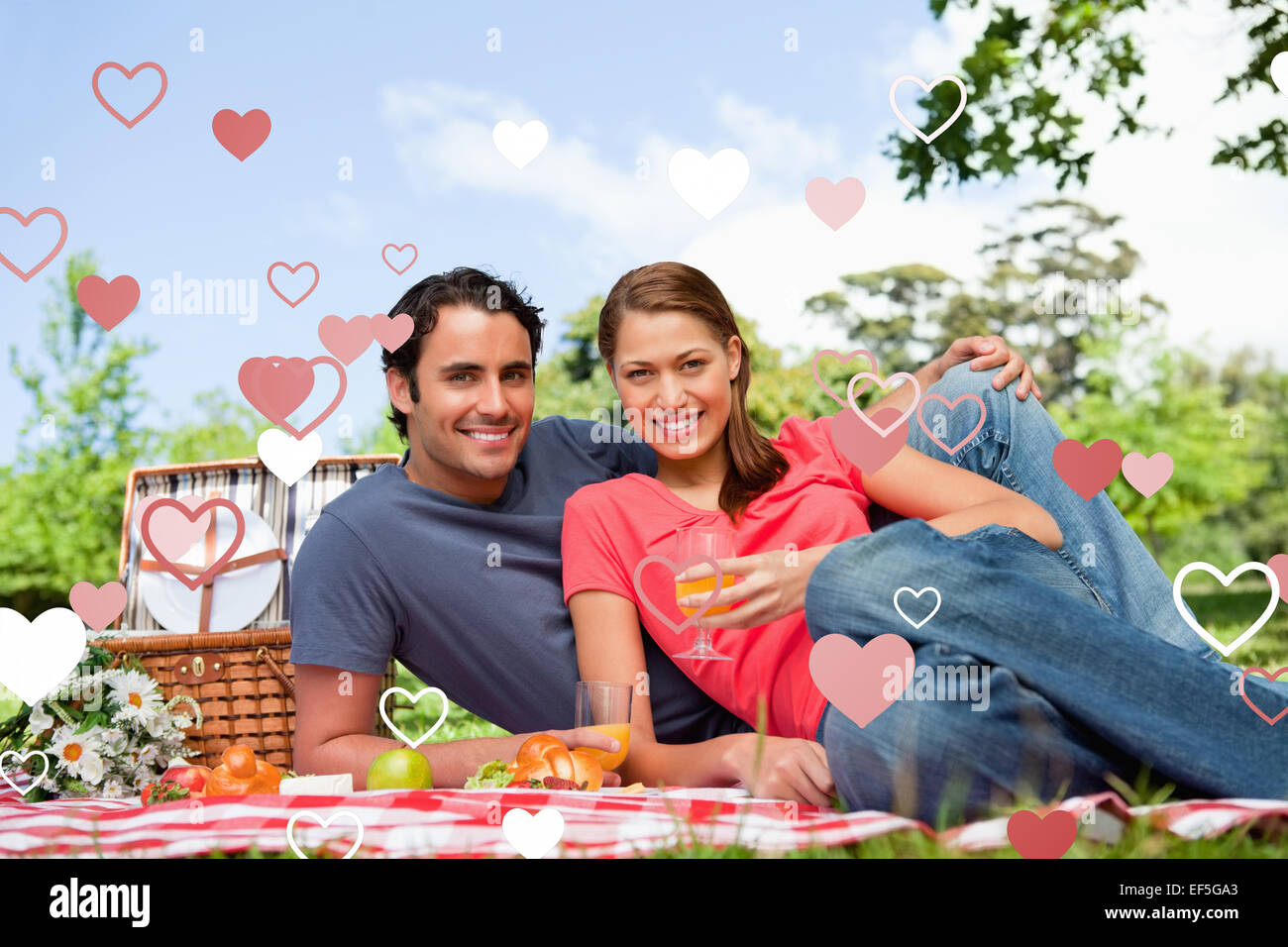 Composite image of two friends looking ahead while they hold glasses as they lie on a blanket Stock Photo