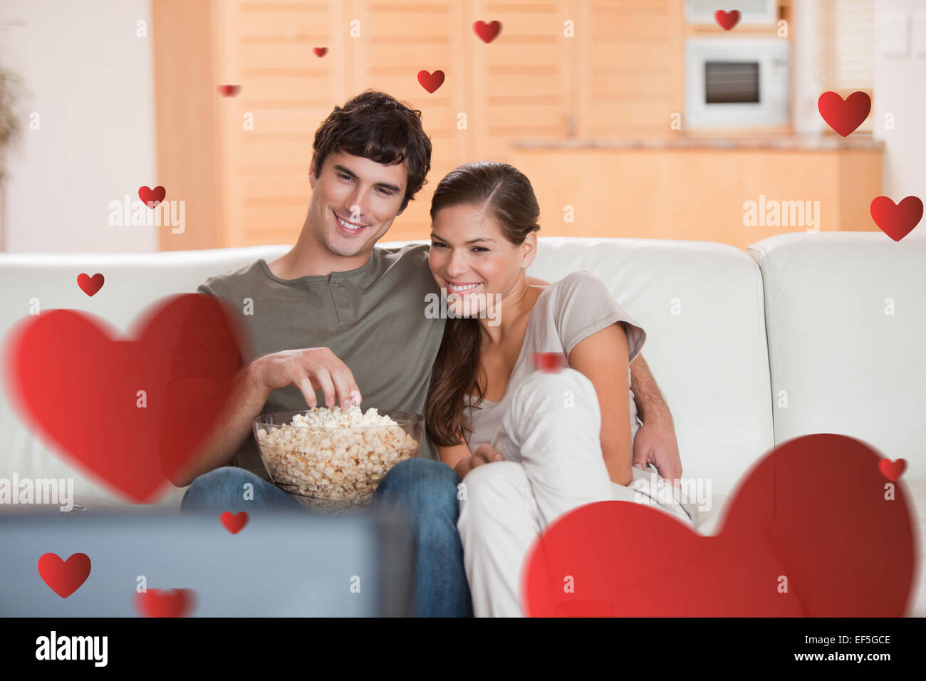 Composite image of couple with popcorn on the sofa watching a movie Stock Photo