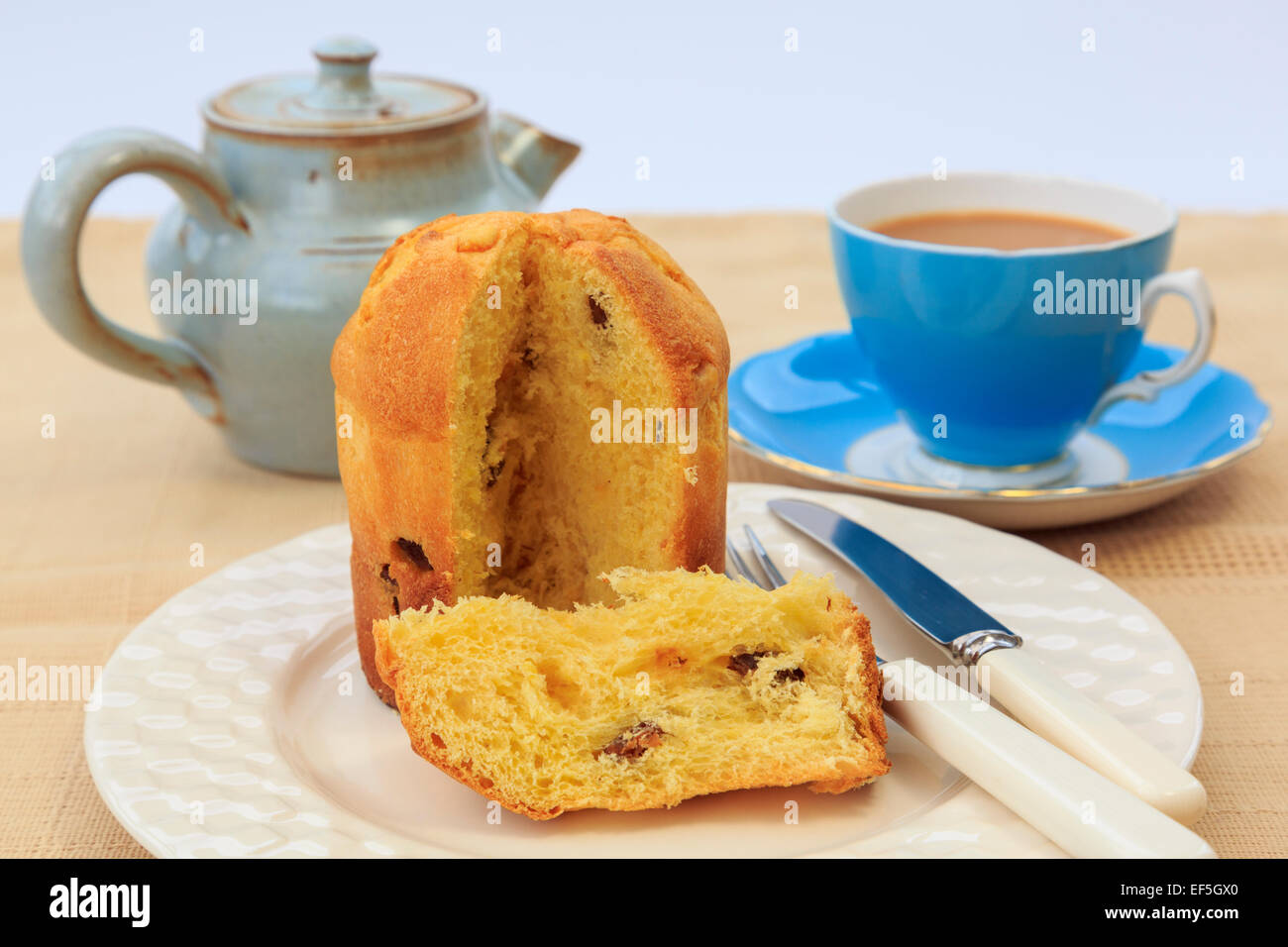 A slice of Panettone Italian Christmas fruit bread cake on a plate with a cup of tea and teapot on a table for afternoon tea. UK Stock Photo