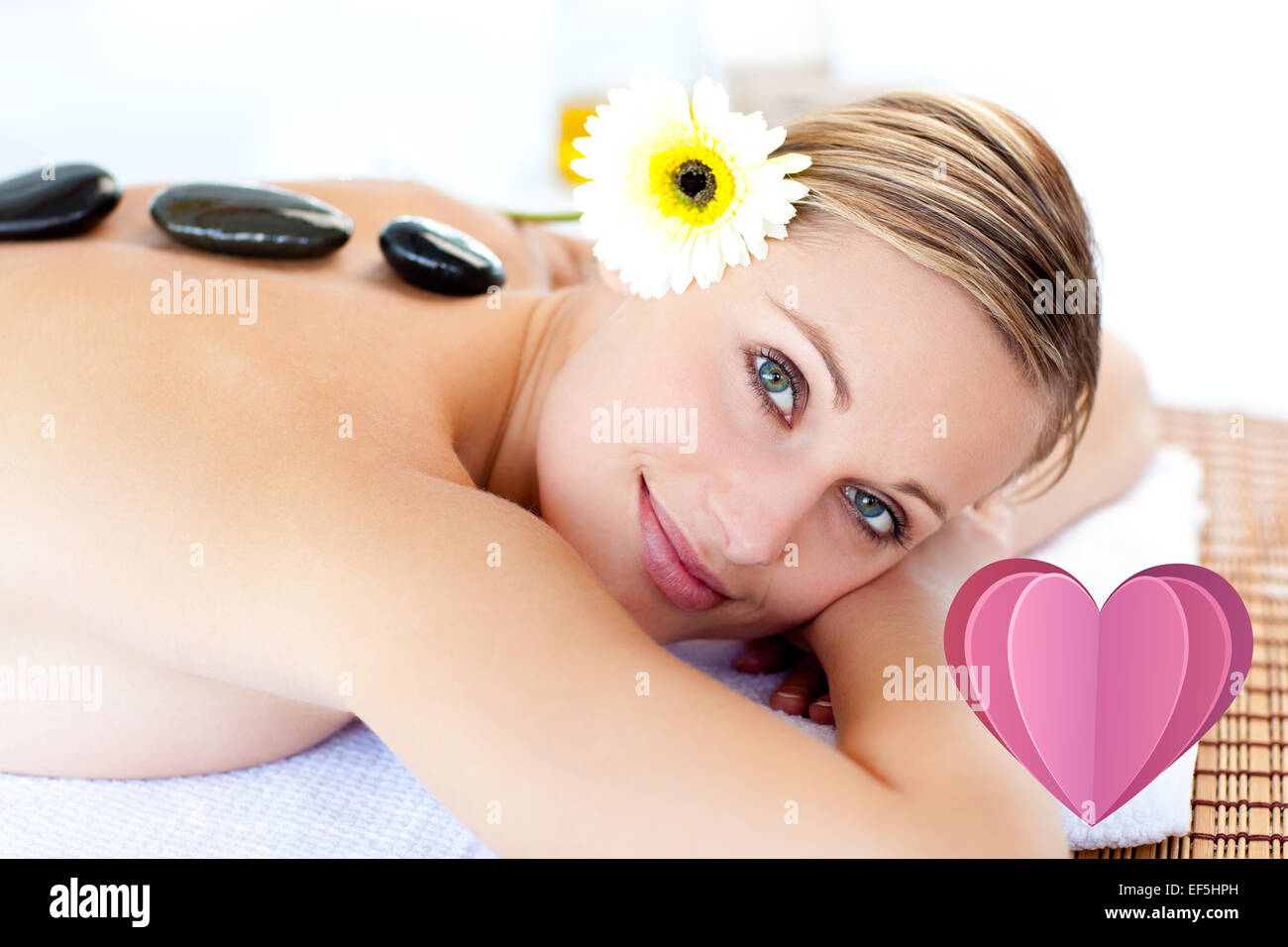 Composite image of glowing young woman with hot stones on her back smiling at the camera Stock Photo