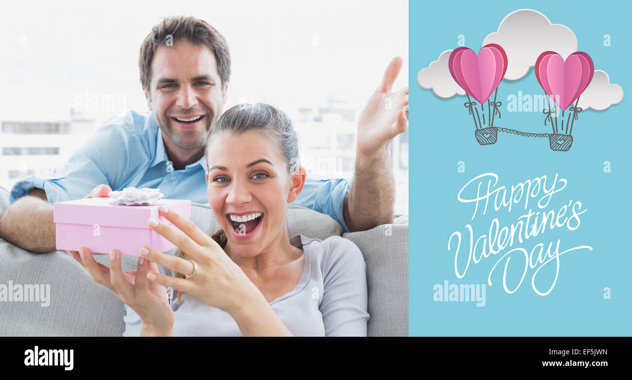 Composite image of man surprising his delighted girlfriend with a pink gift on the sofa Stock Photo