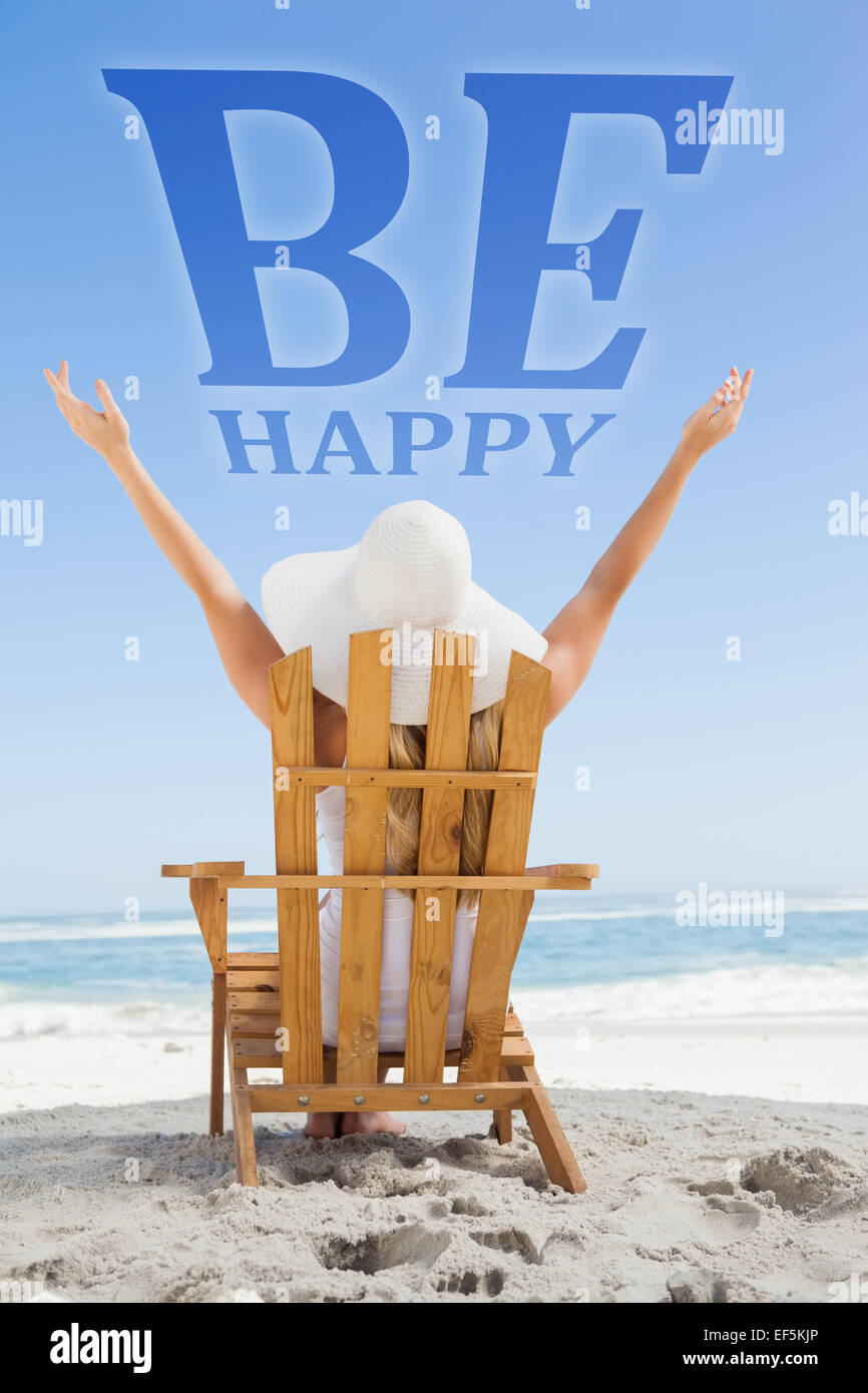 Composite image of woman sitting in deck chair at the beach with arms up Stock Photo