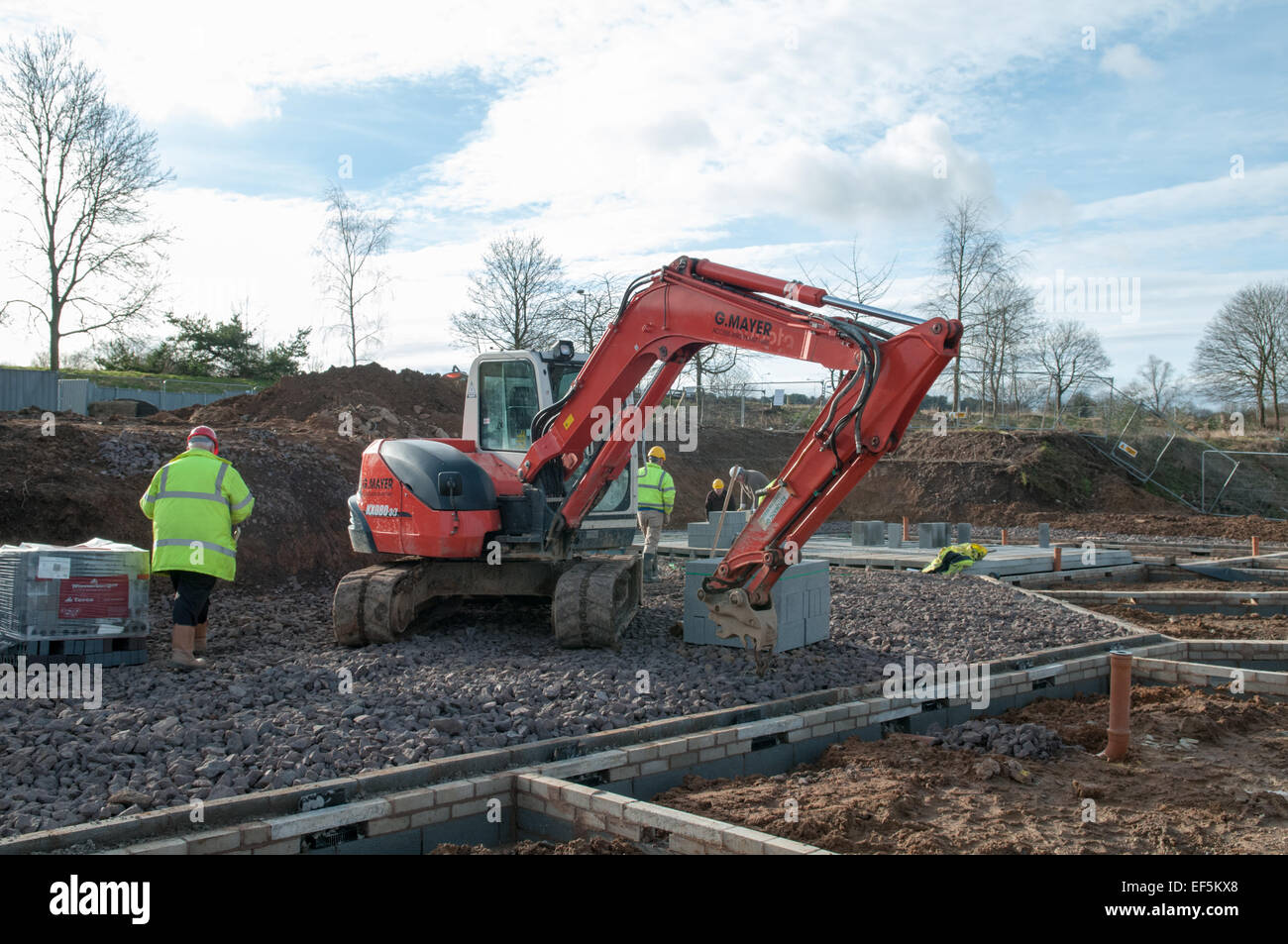 A housing building site with a digger, piles of breeze blocks and builders in hi-viz jackets working on the construction Stock Photo