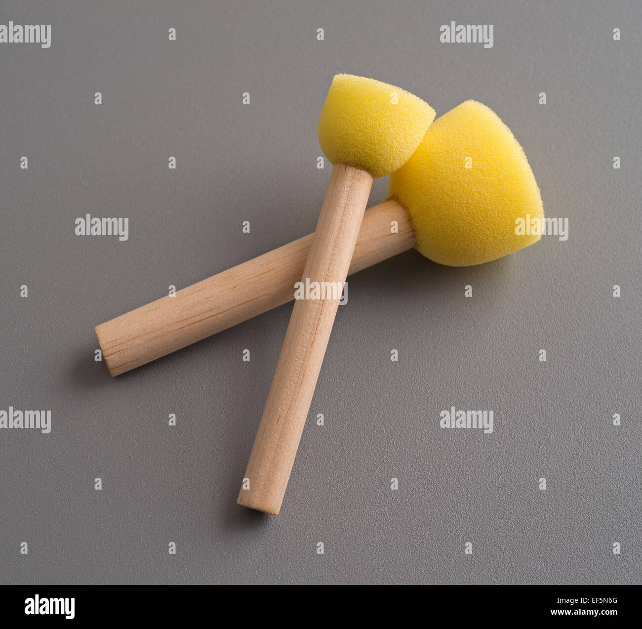 Two small wood handle yellow foam stencil brushes on a gray background. Stock Photo