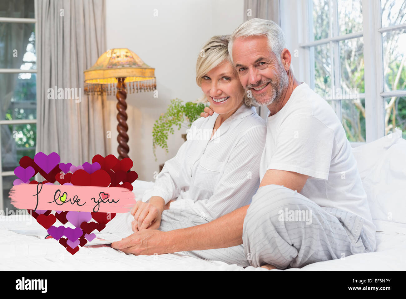 Composite image of portrait of a relaxed happy mature couple with book in bed Stock Photo