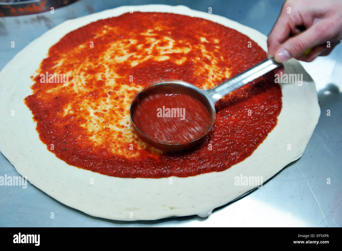 Close up of tomato sauce added to dough to make Pizzas in a takeaway, Leeds Stock Photo
