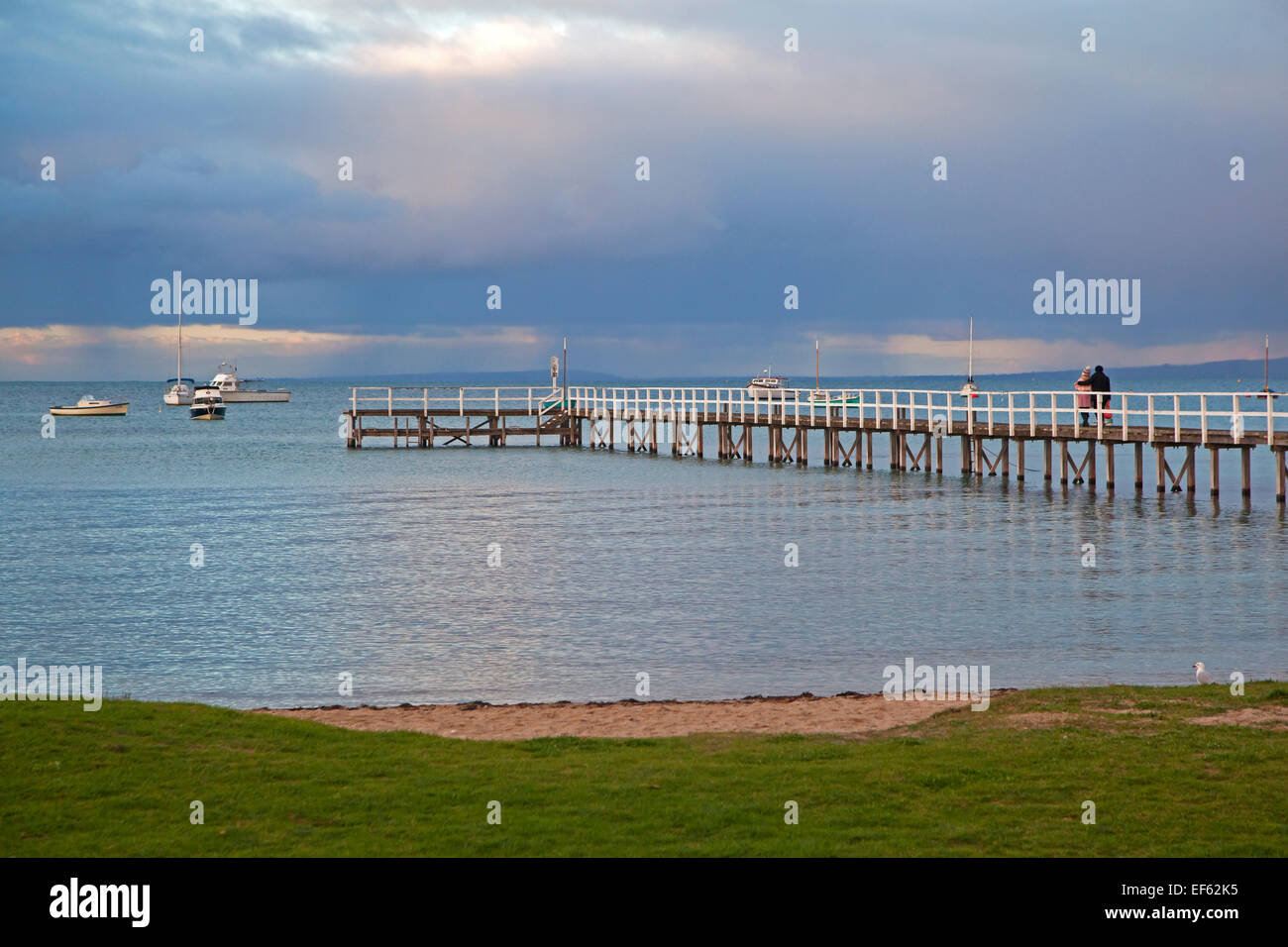 Couple watching sunset from wooden jetty at seaside resort Sorrento in the Port Phillip Bay, Victoria, Australia Stock Photo