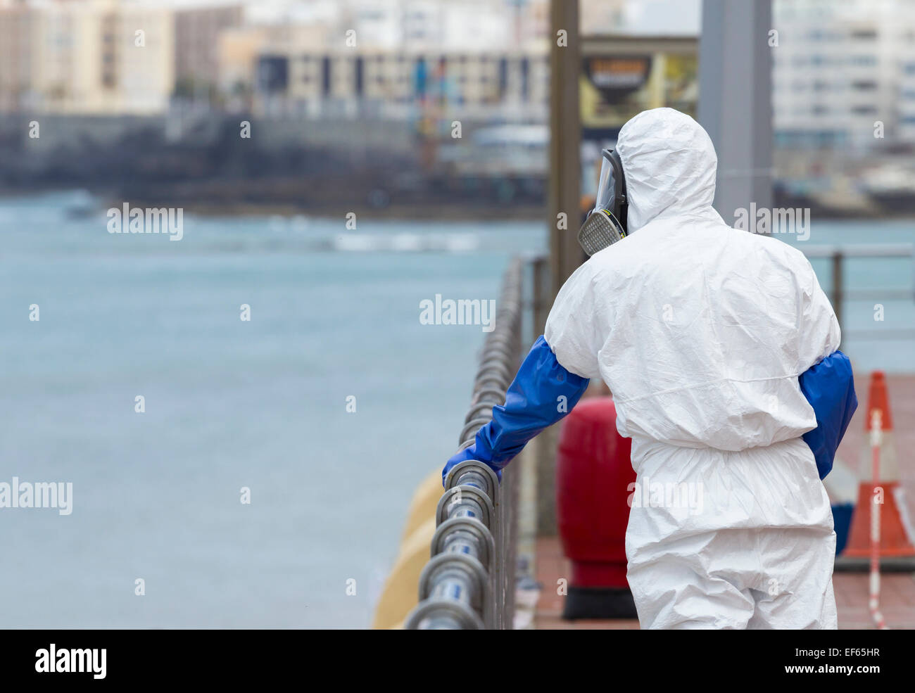 Council worker in protective suit and mask using chemical product to clean Stainless steel railings overlooking beach in Spain Stock Photo