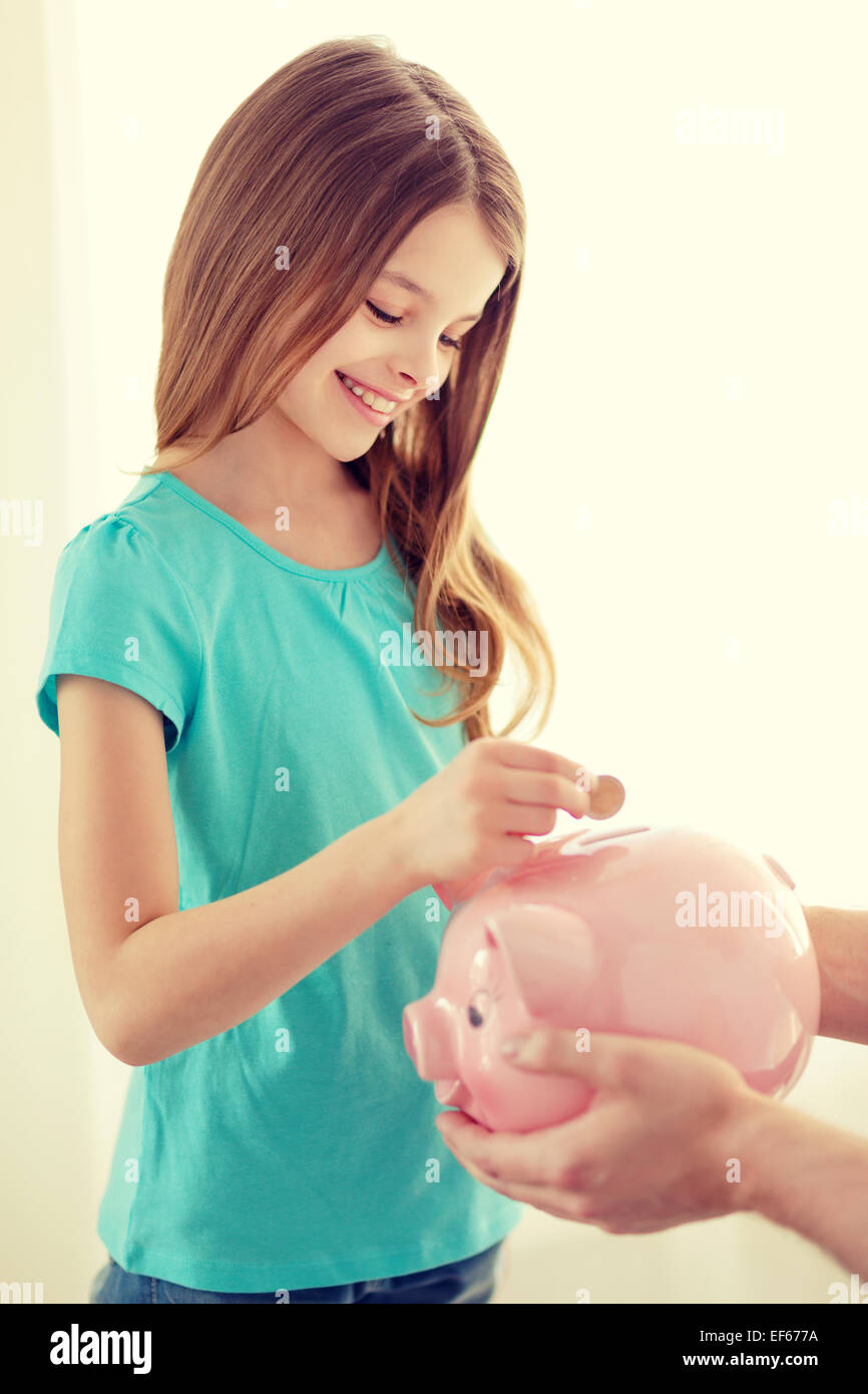 smiling little girl putting coin into piggy bank Stock Photo - Alamy