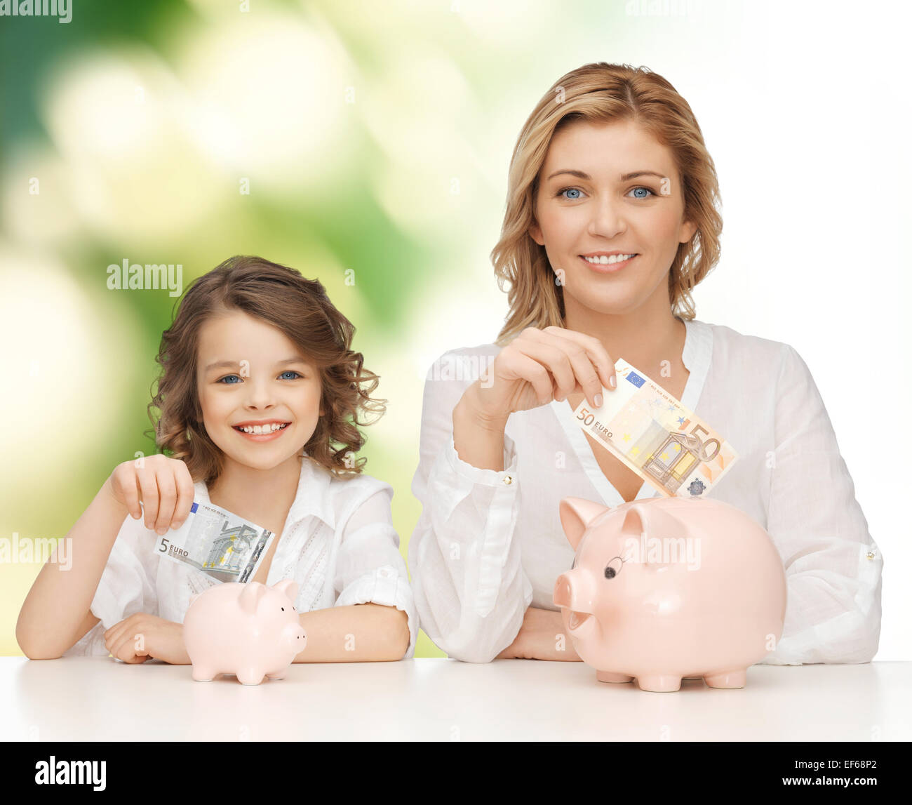 mother and daughter putting money to piggy banks Stock Photo - Alamy