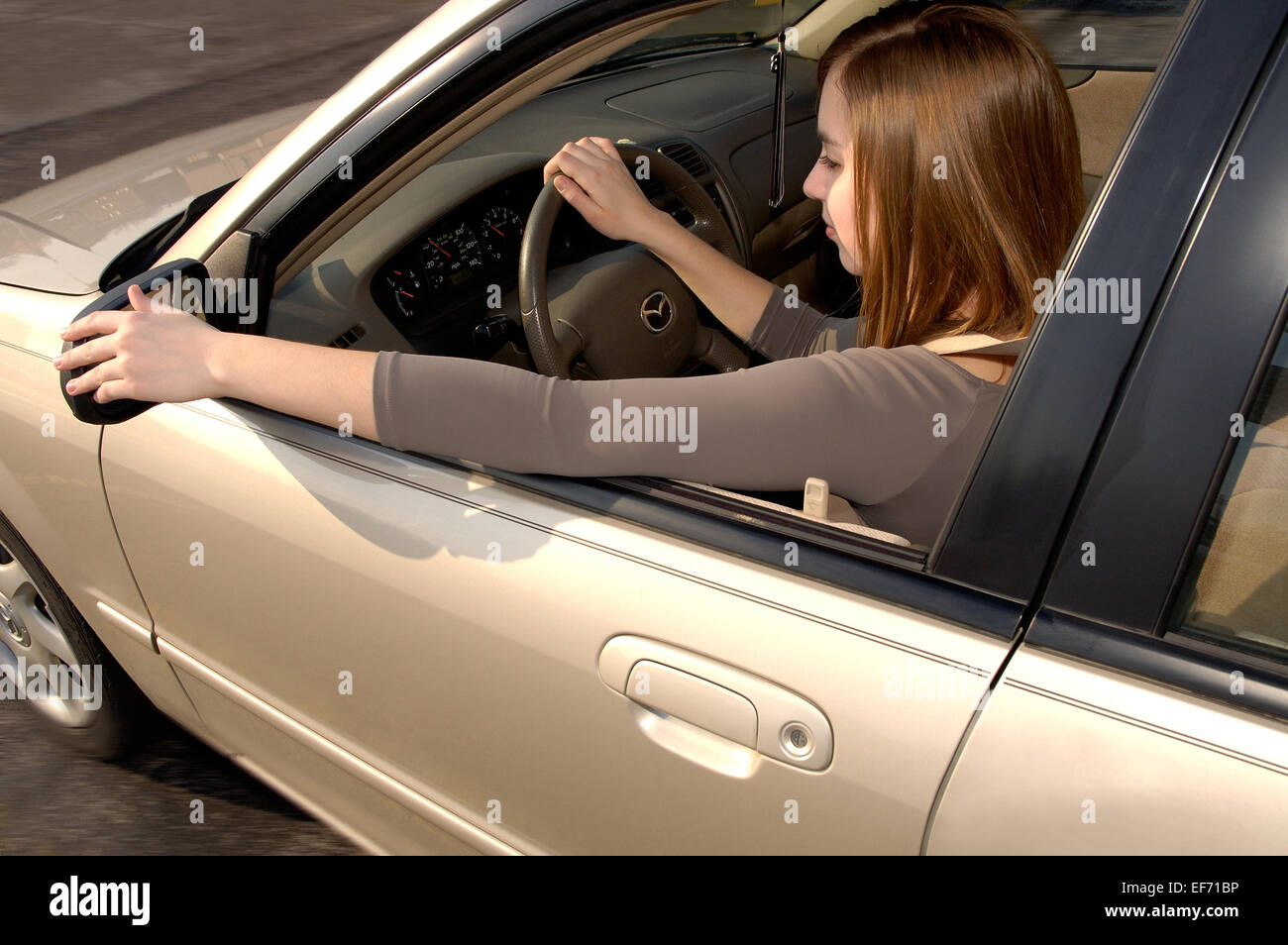 Teenage driver behind the wheel of a car, adjusting the rear view mirror. Stock Photo