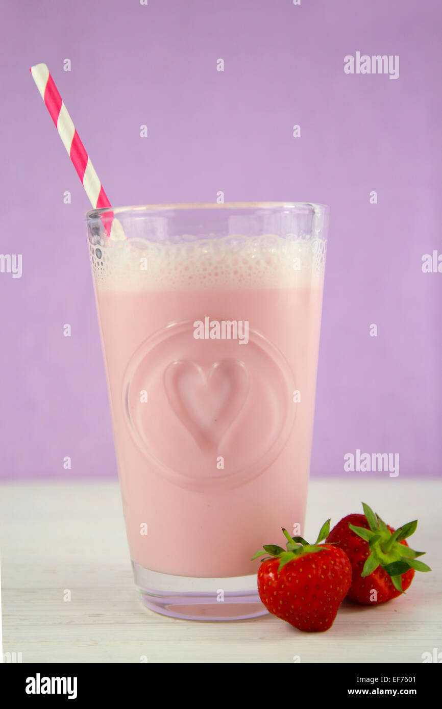Strawberry milkshake in a heart embelished glass with a candy striped paper  straw. Strawberries at base of glass Stock Photo - Alamy