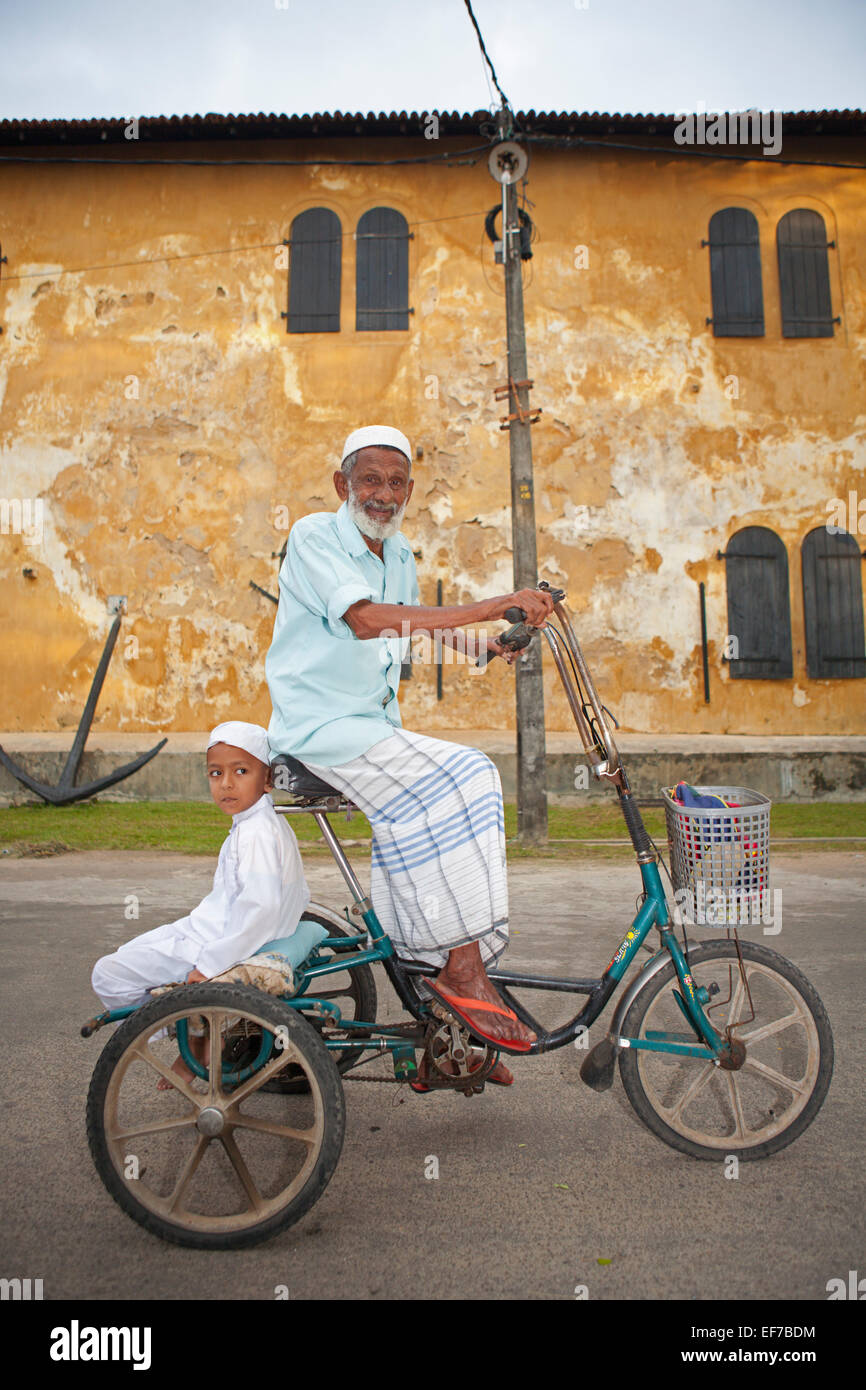 ELDERLY SRI LANKAN MAN AND CHILD CYCLING IN GALLE FORT Stock Photo