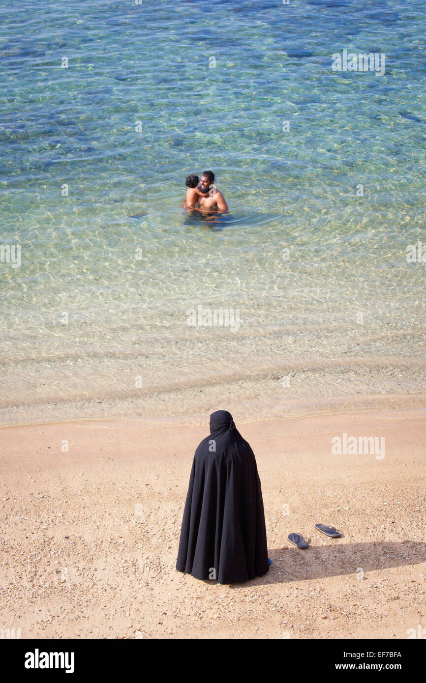 MUSLIM MOTHER IN BURKA WATCHING HUSBAND AND CHILD SWIM Stock Photo