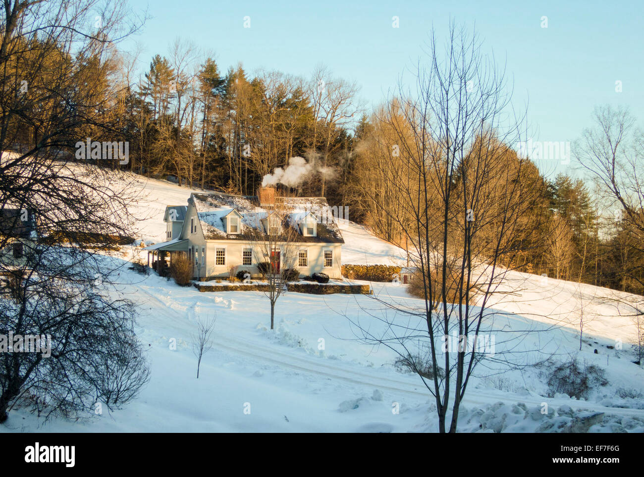 Winter scenic of a Cape-style, restored home with a smoking chimney in Vermont, United States of America. Stock Photo