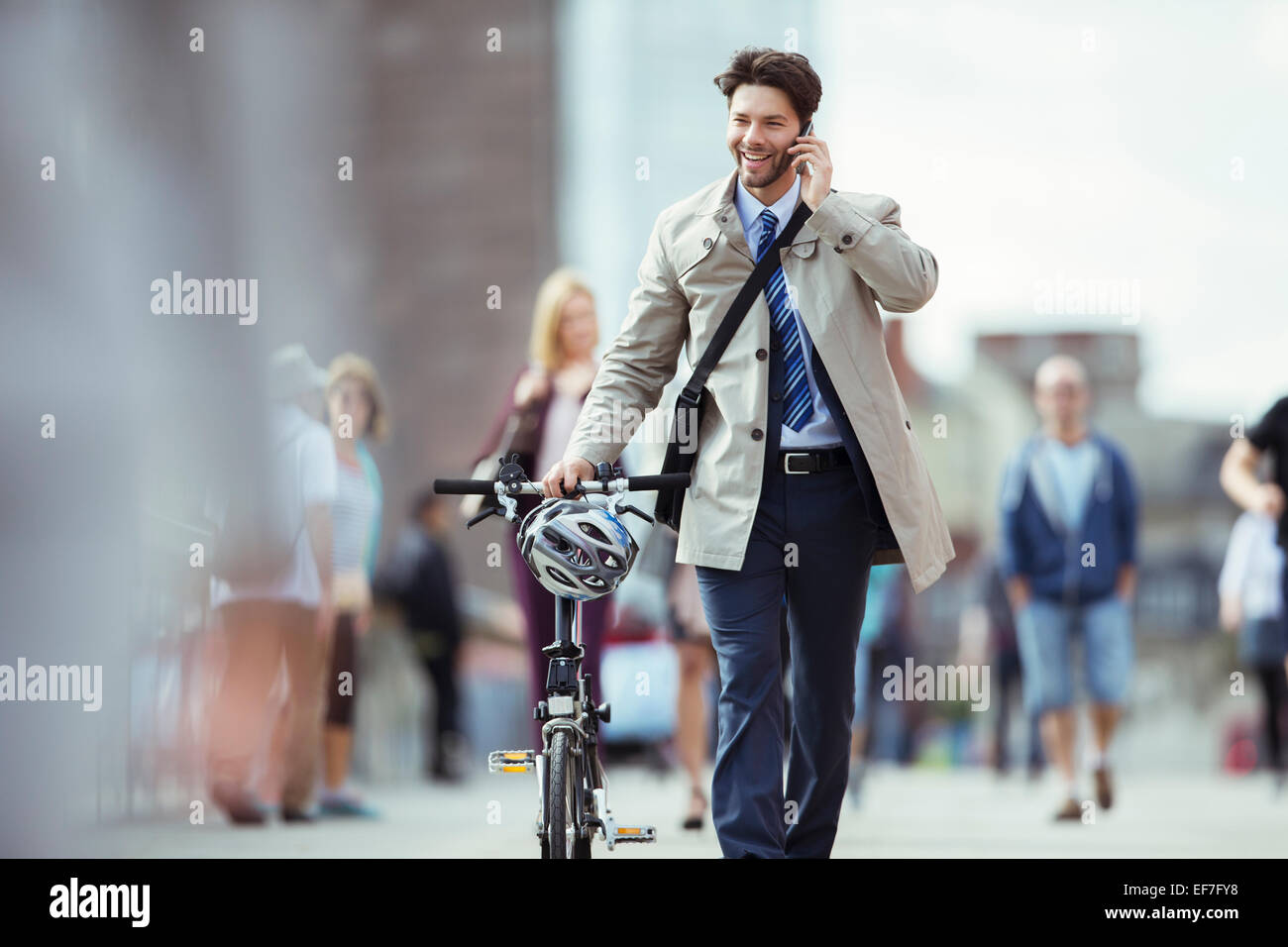 Businessman talking on cell phone pushing bicycle in city Stock Photo