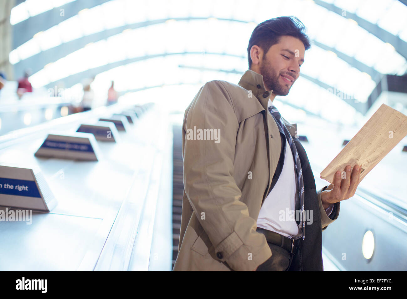 Businessman reading newspaper on escalator Stock Photo