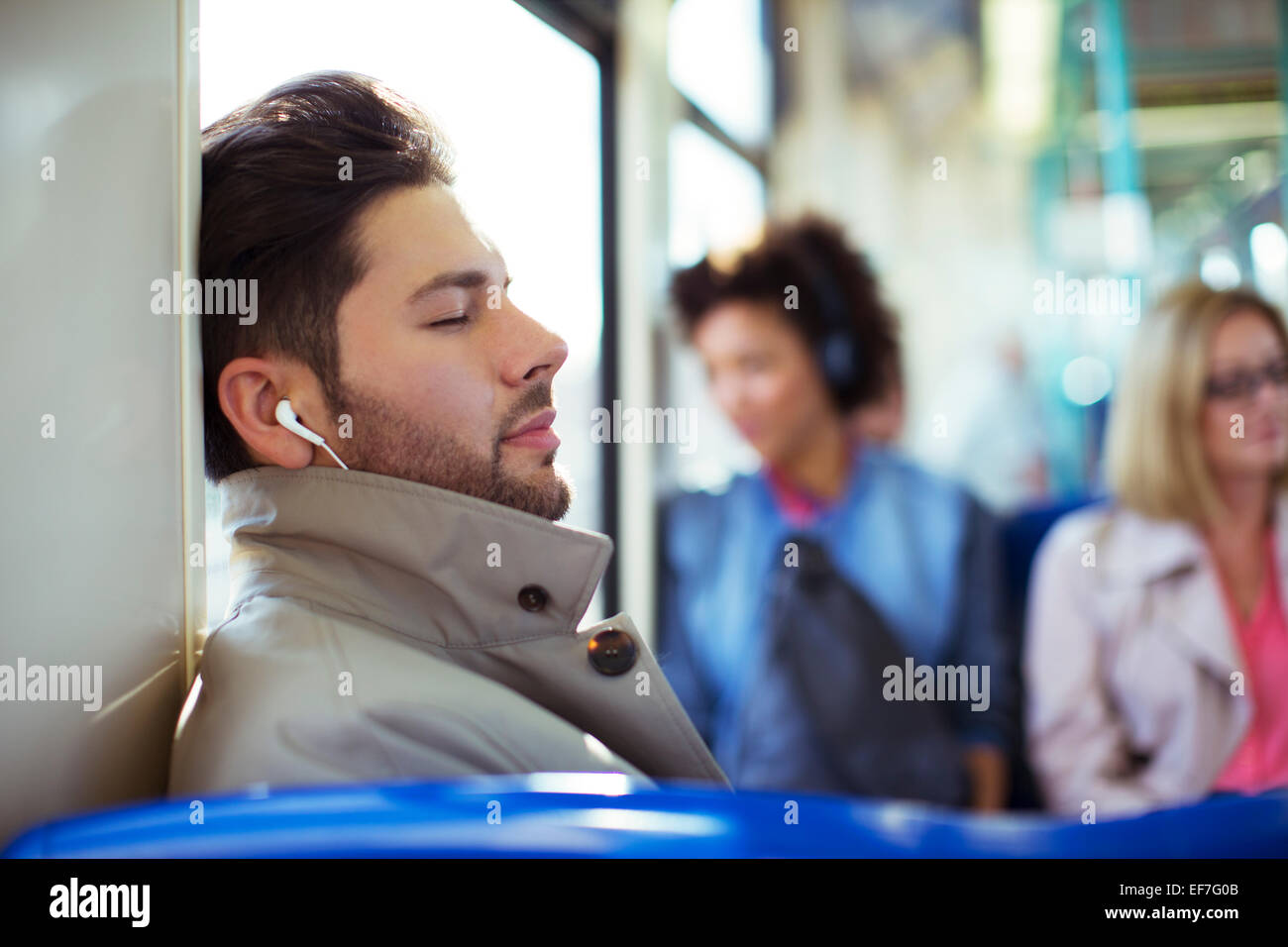 Businessman napping and listening to earbuds on train Stock Photo