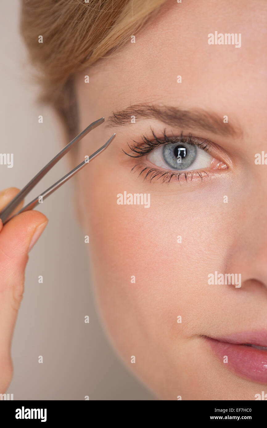 Beautiful woman plucking eyebrow with tweezers Stock Photo