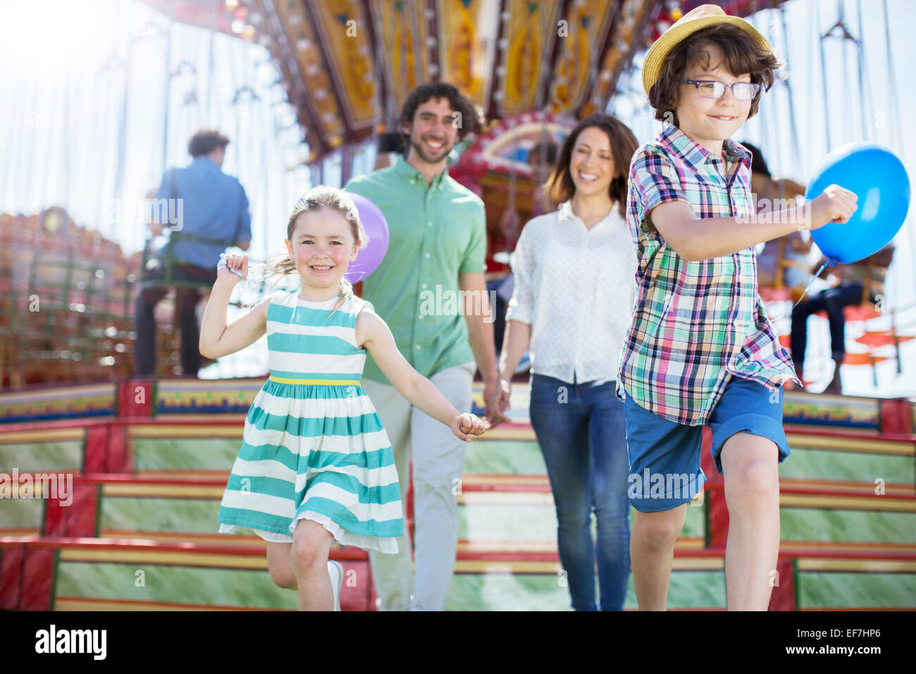 Children running in front of carousel, parents following them Stock Photo