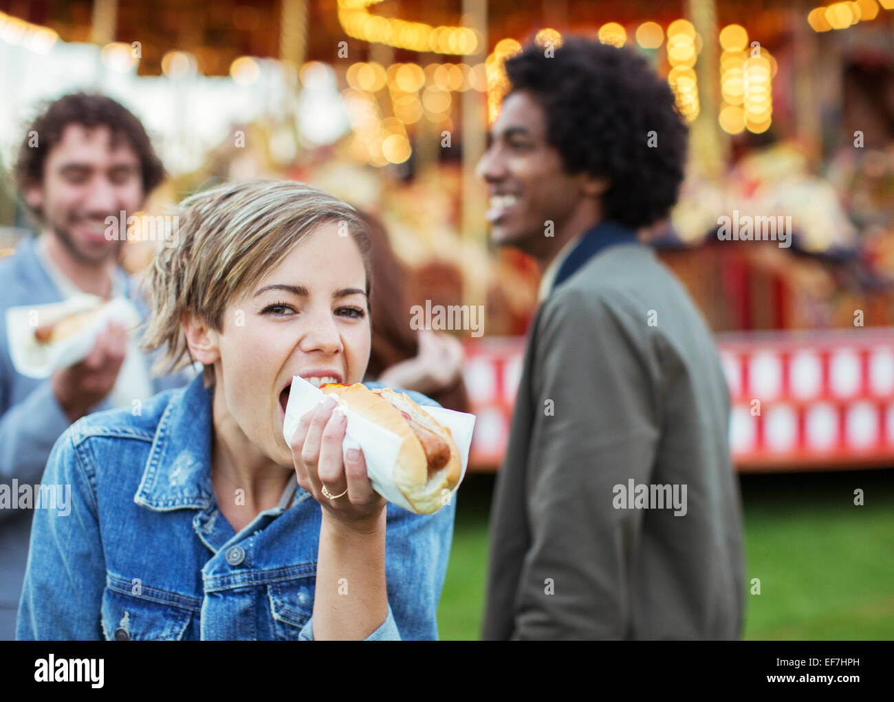 Three young people eating hot-dogs in amusement park Stock Photo