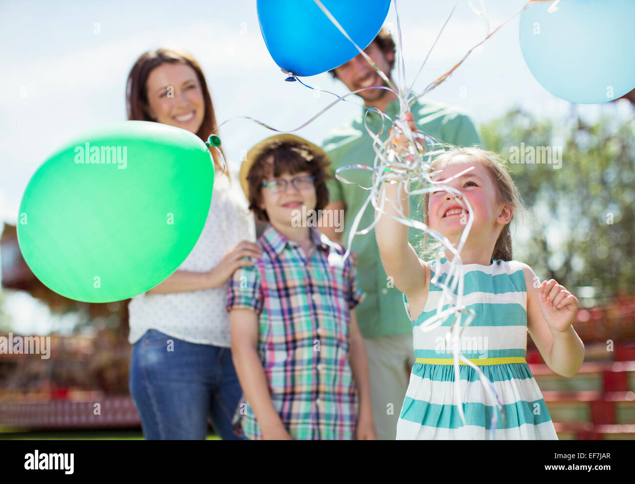 Young girl holding bunch of balloons, family standing behind her Stock Photo