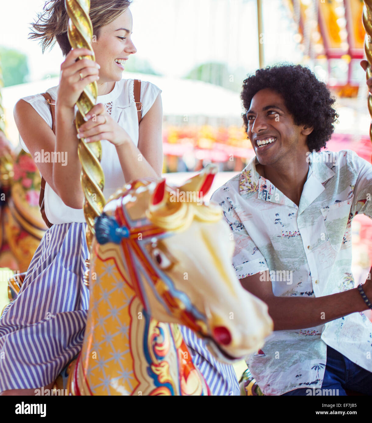 Young multiracial couple smiling on carousel in amusement park Stock Photo