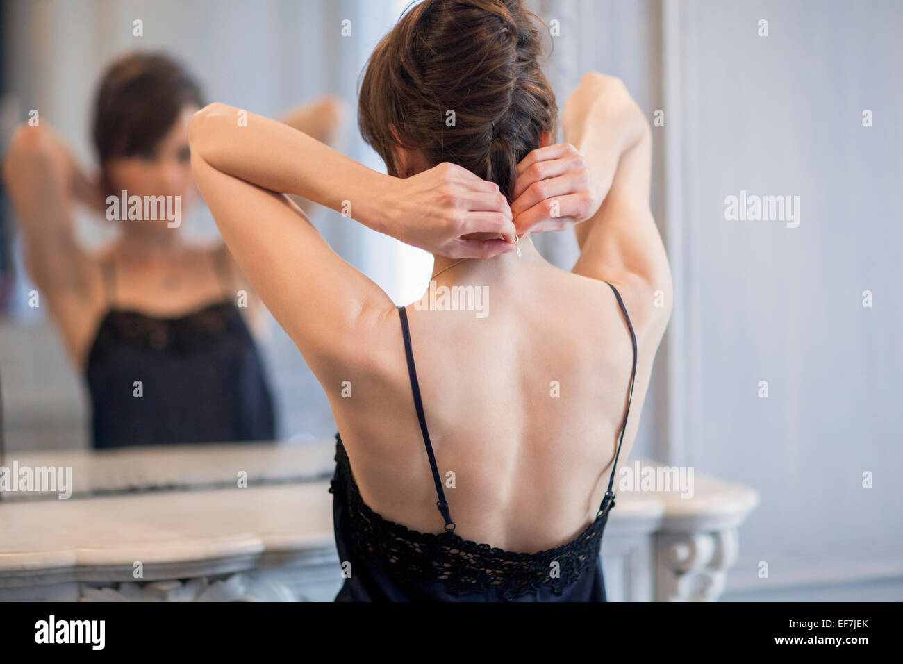 Woman putting on necklace in front of mirror Stock Photo