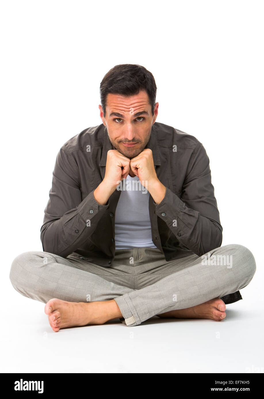 Thoughtful man sitting on the floor, looking at camera, with the hands under his chin Stock Photo