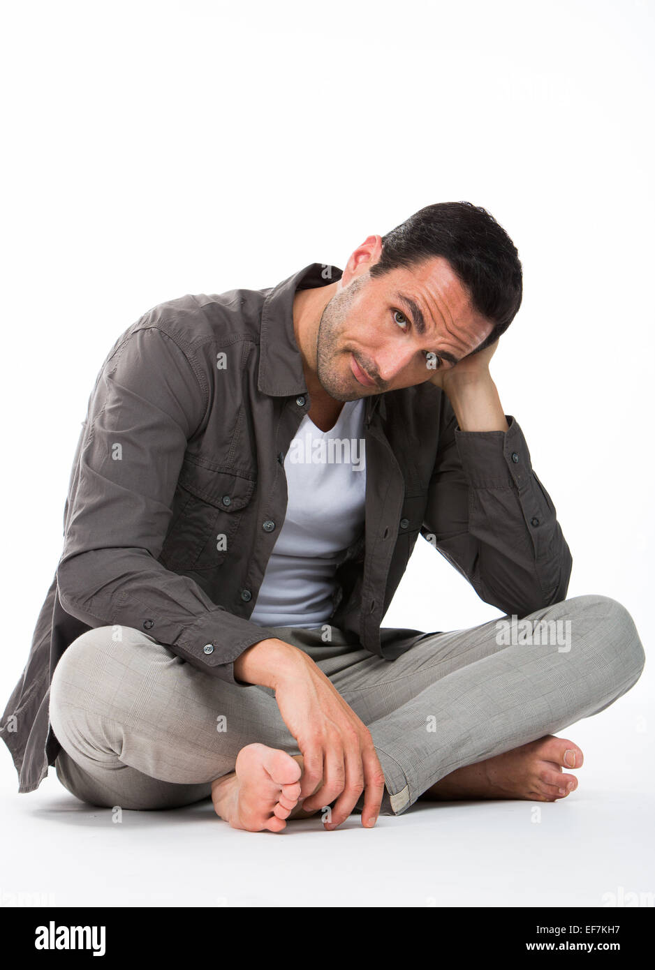 Thoughtful man sitting on the floor, looking at camera and holding his head with one hand Stock Photo