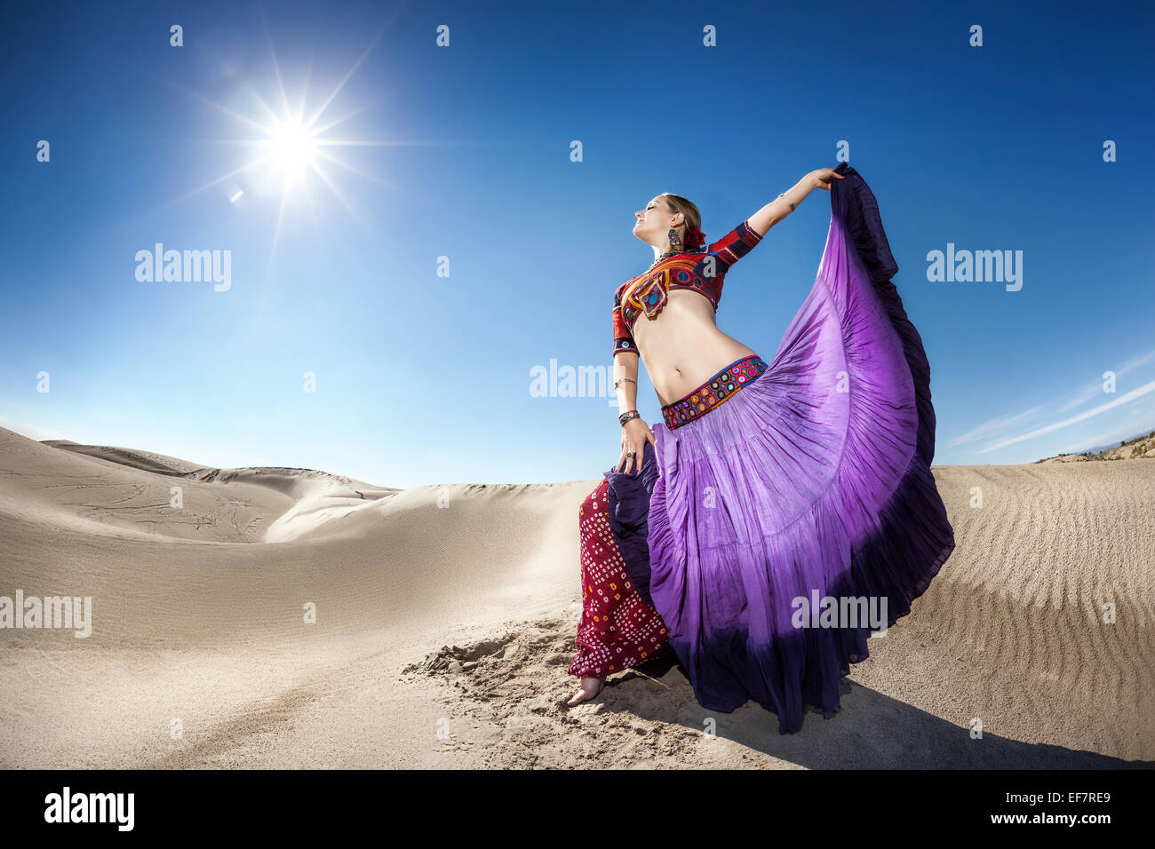 Woman in violet skirt dancing in the desert at blue sky Stock Photo