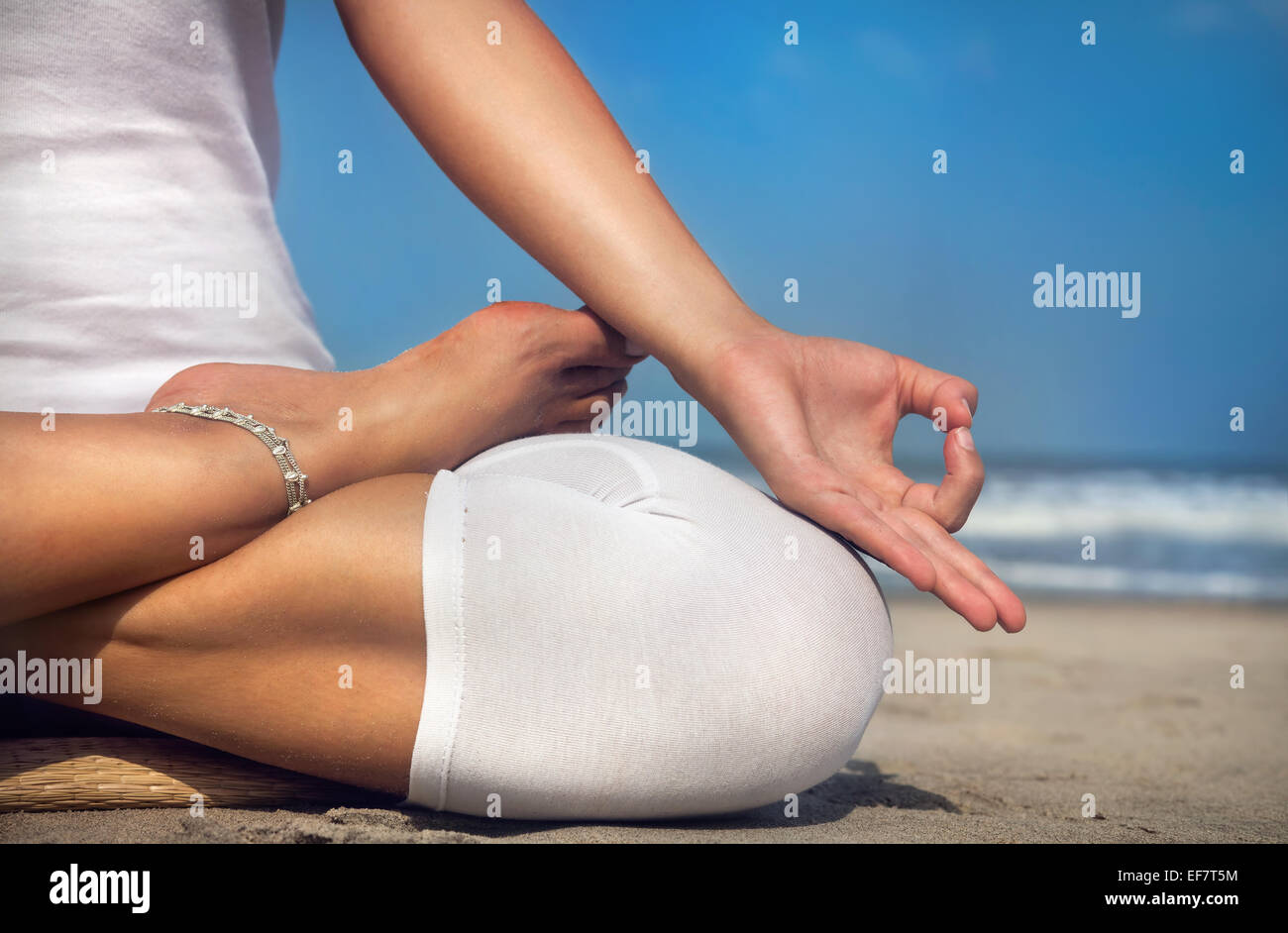 Woman doing yoga meditation in white costume on the beach in Goa, India Stock Photo