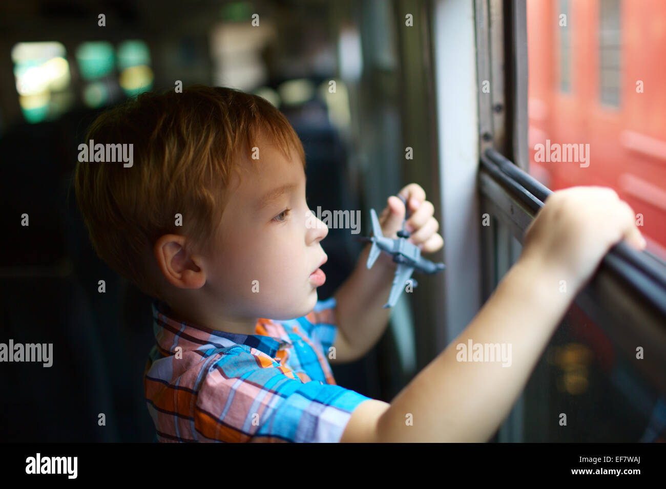Little boy with toy looking out of train window Stock Photo