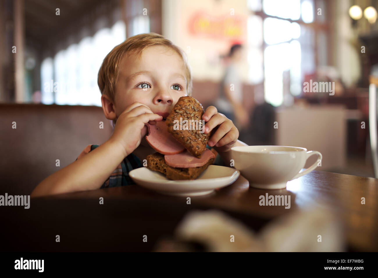 Little child having lunch with sandwich and tea in cafe Stock Photo