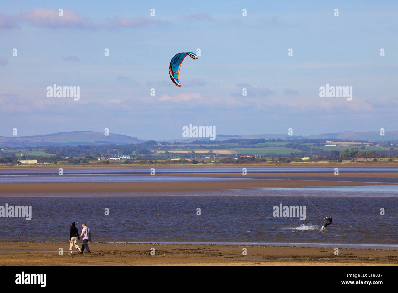 Couple walking past Kitesurfer. Solway Coast, Cumbria, England, United Kingdom. Stock Photo