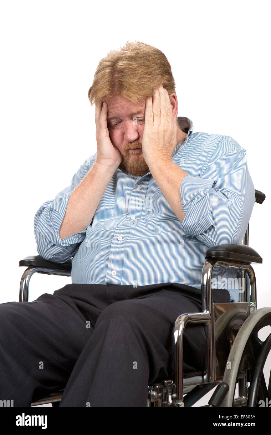 Worried and depressed disabled man in a wheelchair holds his head in his hands. Stock Photo