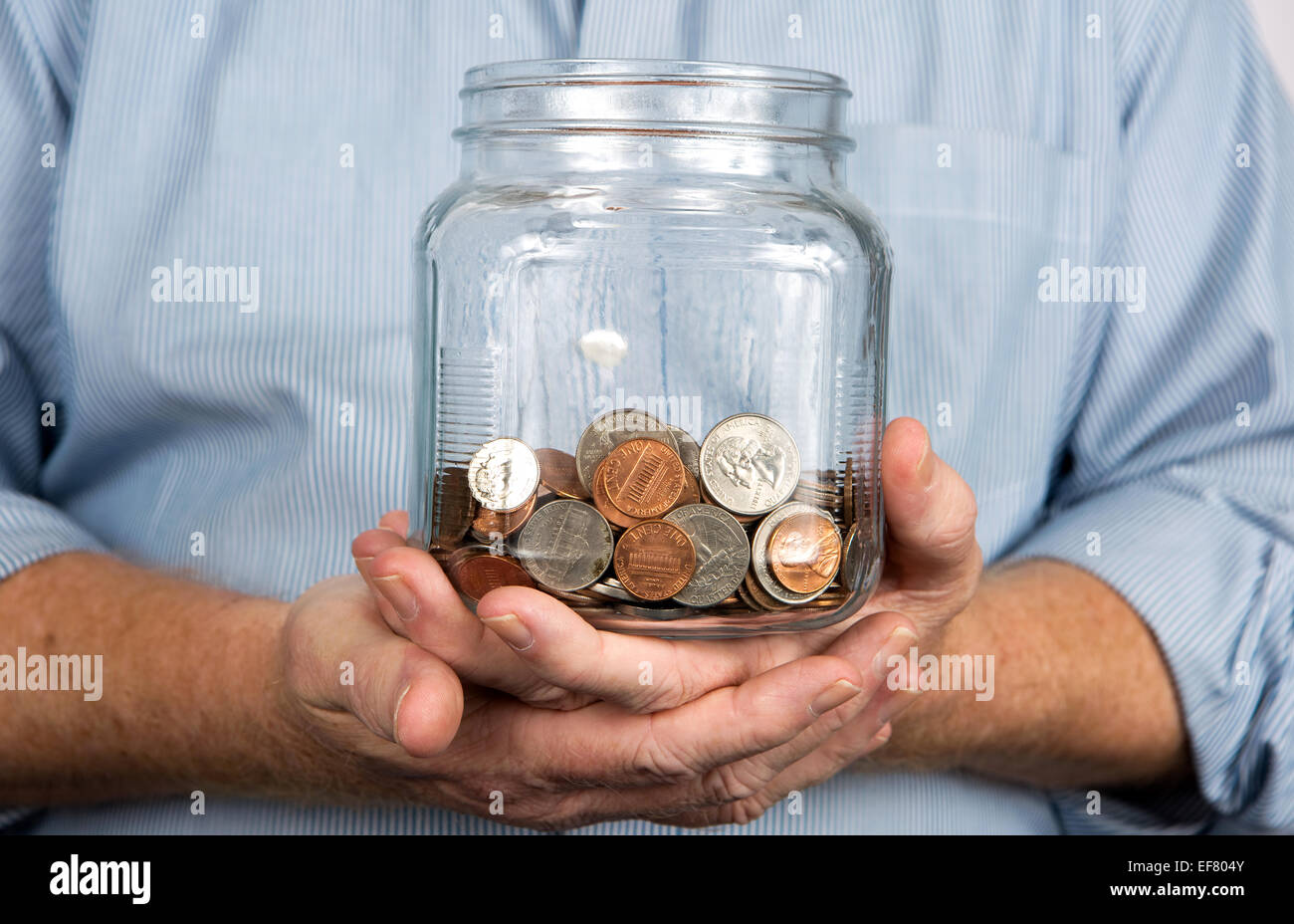 Man holds a glass jar containing United States coins and money. Stock Photo