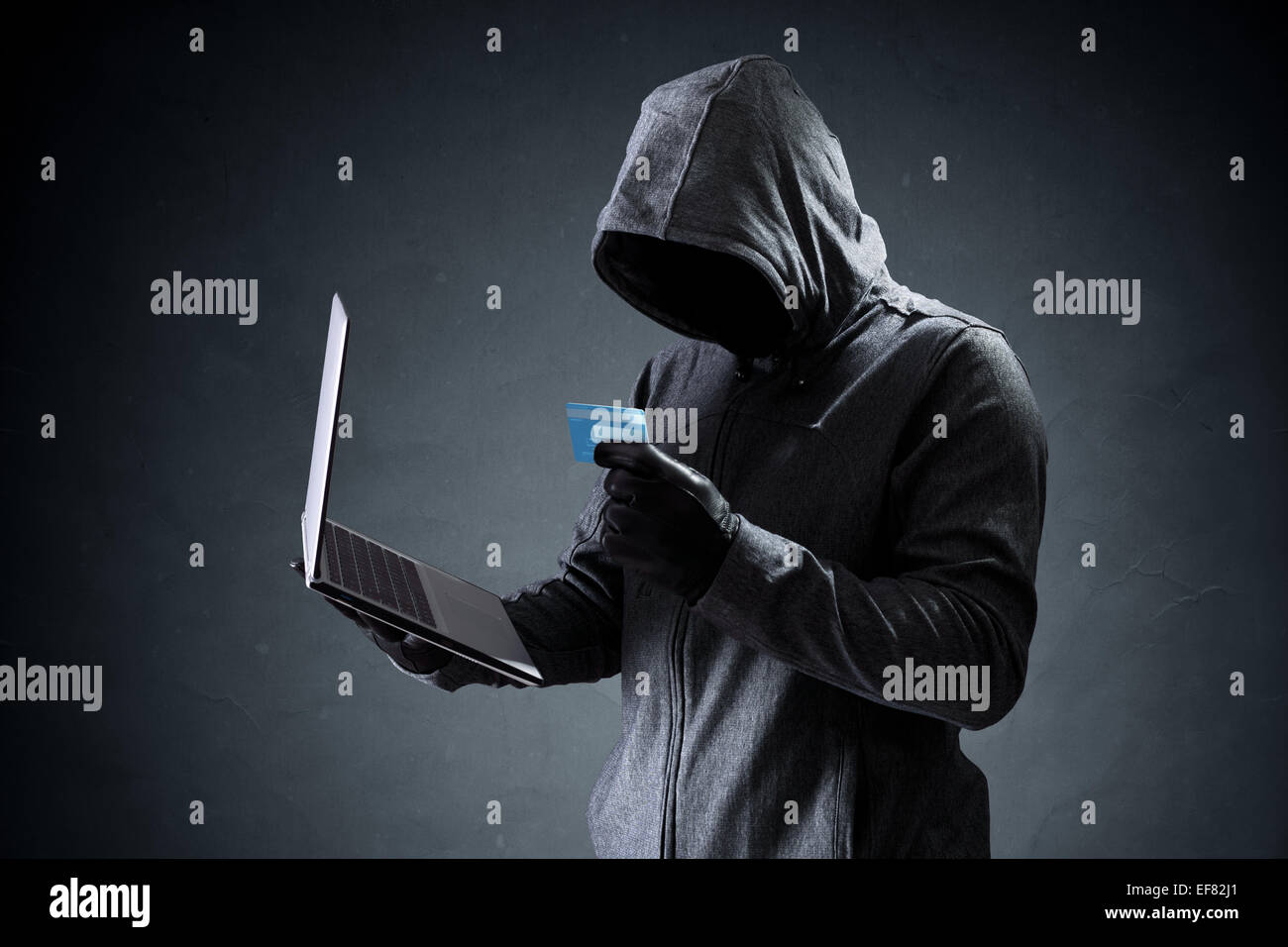 Computer hacker with credit card stealing data from a laptop concept for network security, identity theft and computer crime Stock Photo