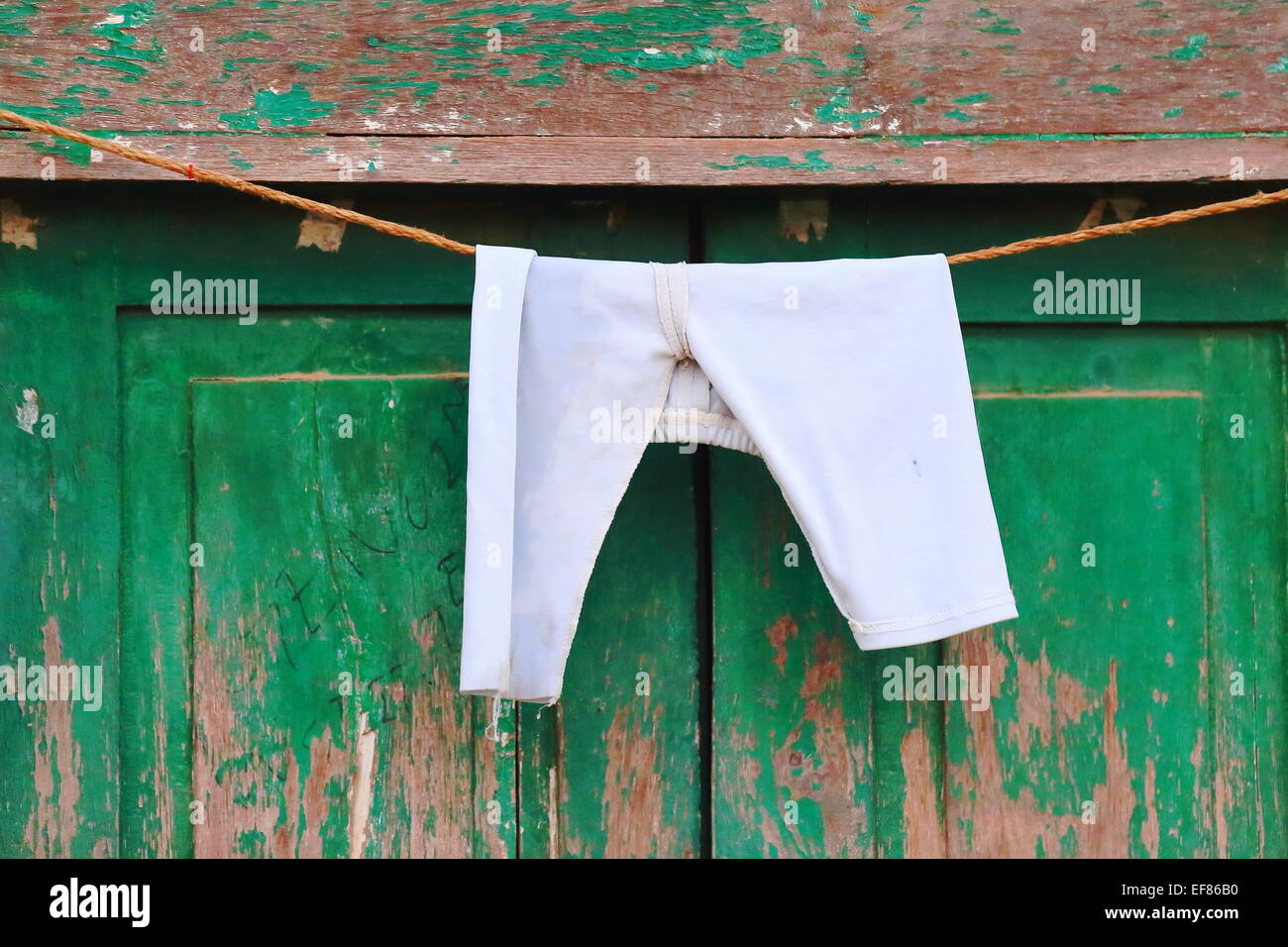 White sports pants at dry  hanging from a rope before a green door showing some hand script on the facade of a nepalese townhome Stock Photo