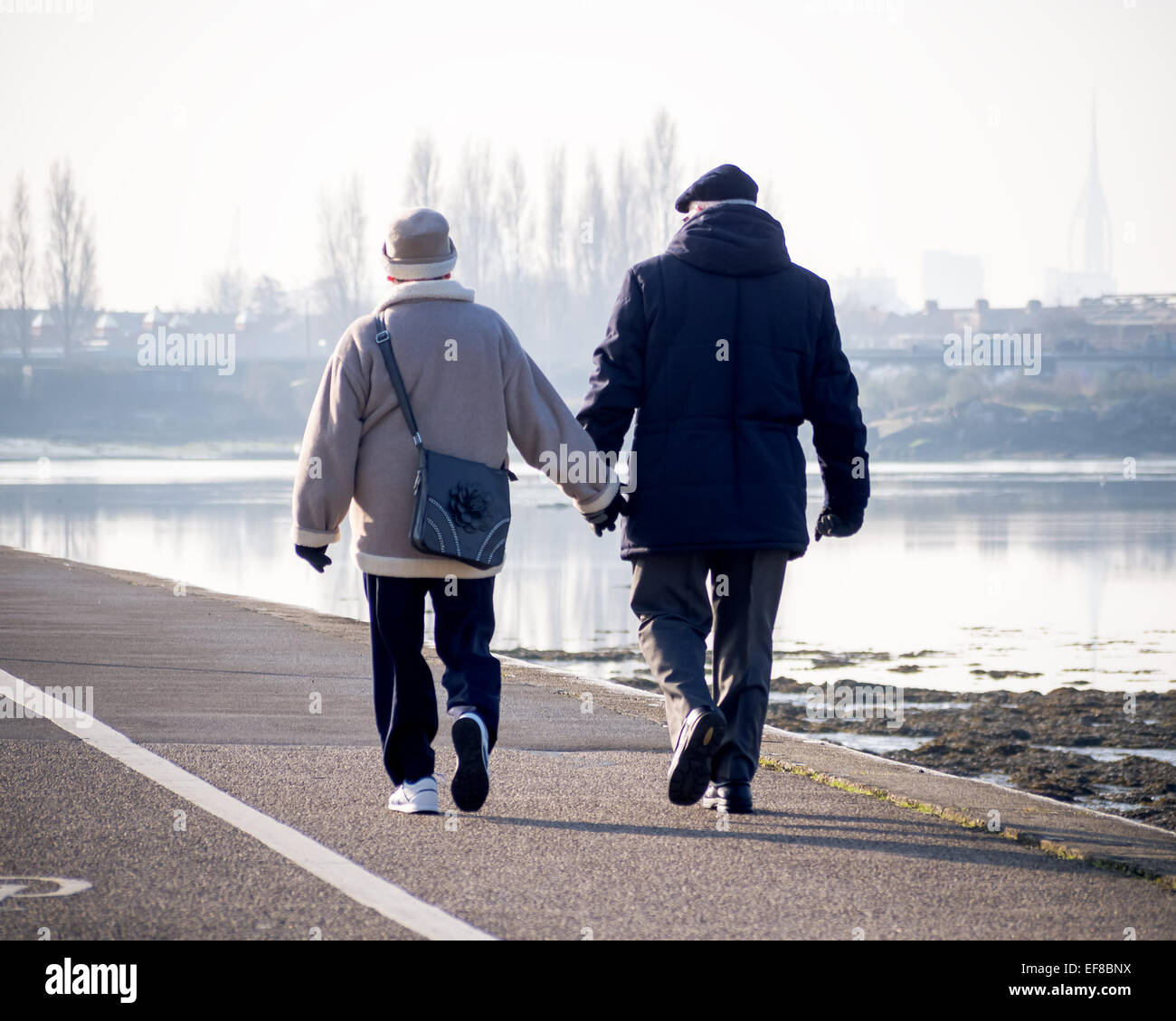 A senior couple walk hand in hand along the shore line of tipner lake, portsmouth Stock Photo