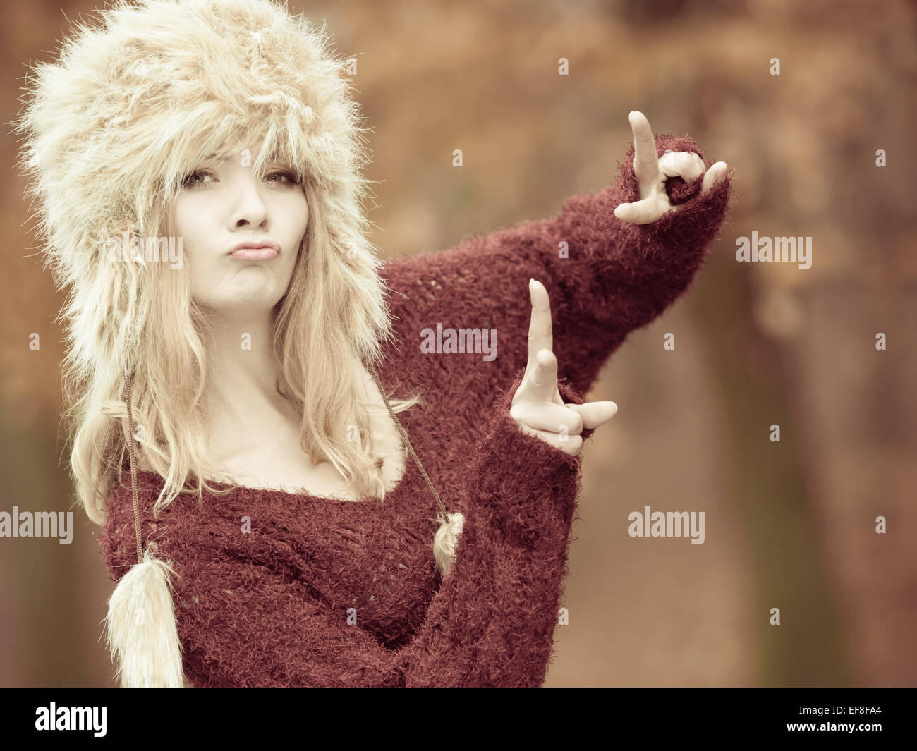 Autumn or winter fashion. Happy funny woman in fashionable wintertime clothes fur cap having fun outdoor making victory hand ges Stock Photo
