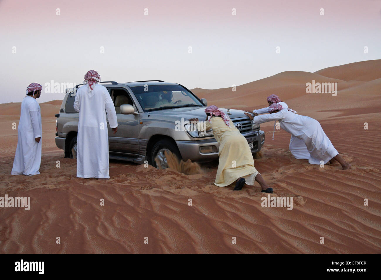 Arab men pushing car stuck in sand, Liwa, Abu Dhabi, United Arab Emirates Stock Photo