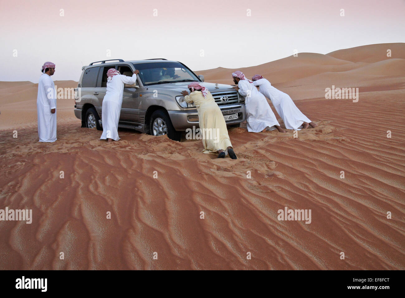 Arab men pushing car stuck in sand, Liwa, Abu Dhabi, United Arab Emirates Stock Photo