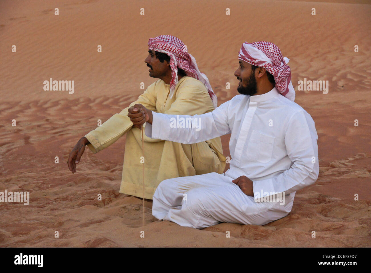 Arab men in traditional dress sitting in sand dunes of Liwa, Abu Dhabi, UAE Stock Photo