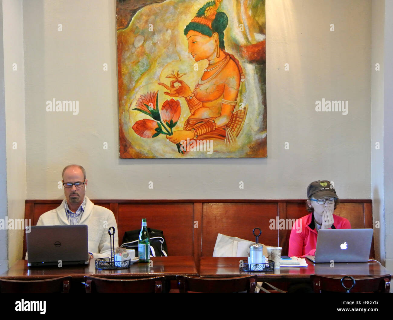 man and woman work on their laptops at Sausalito Coffee shop under Buddha with lotus flower painting by local artist Stock Photo